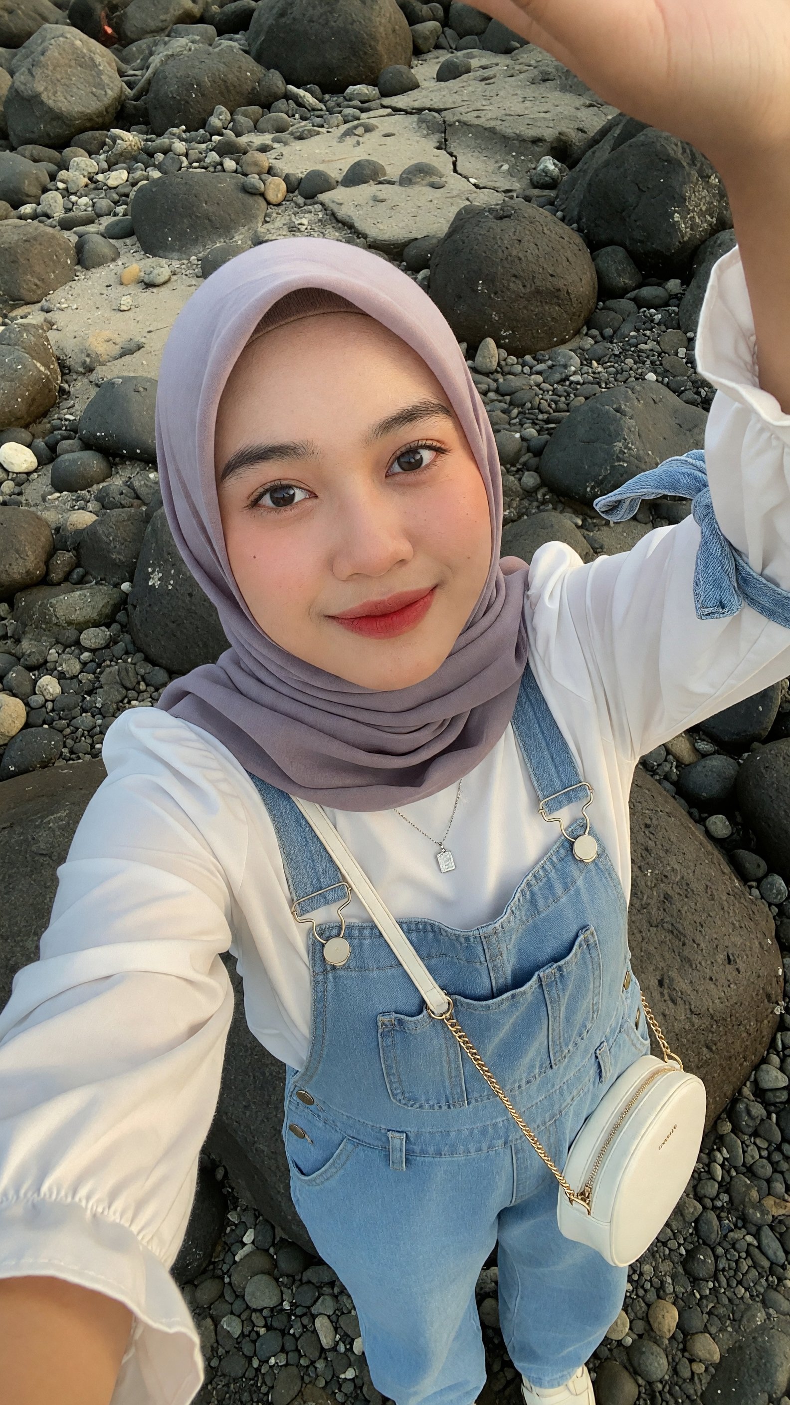 Young hijabi woman selfie on rocky beach in denim